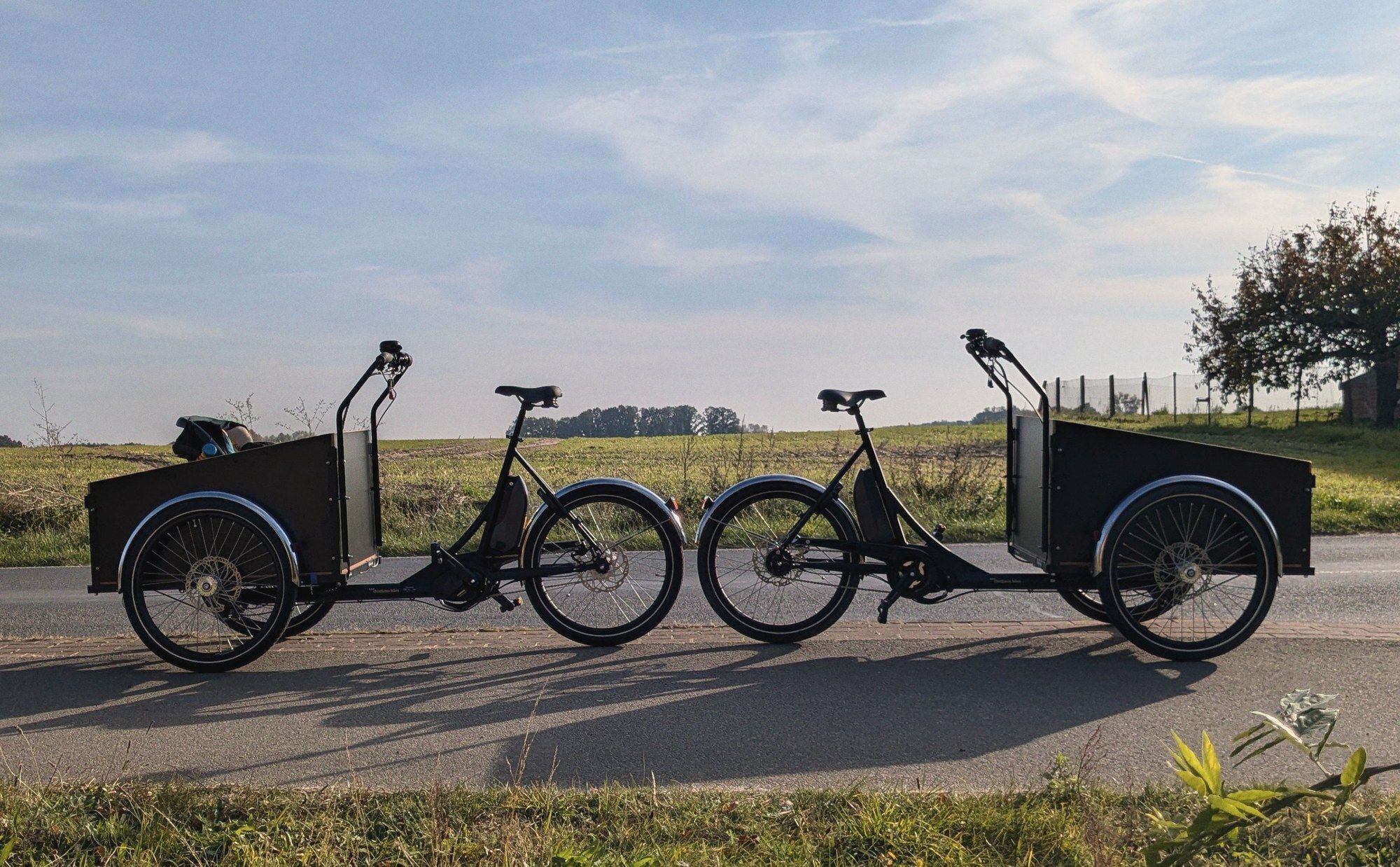 Zwei schwarze E-Lastenräder mit Transportkisten am Rand einer Landstraße