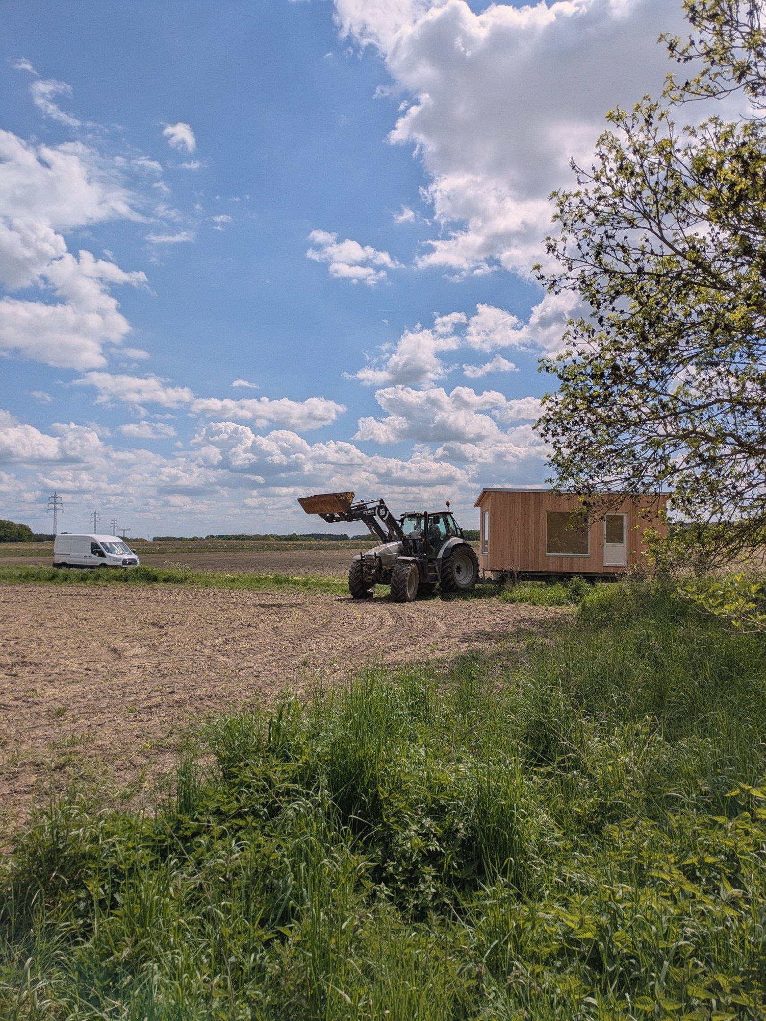Ein Traktor zieht den LandAnker über einen frisch bestellten Acker, am Feldrand steht der Transporter