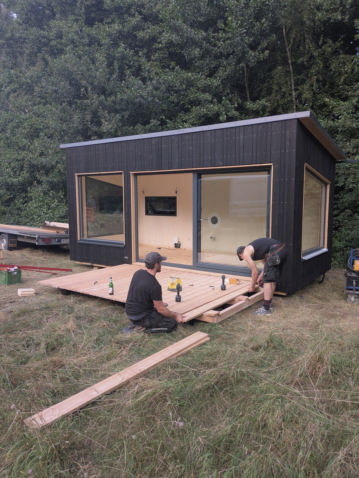 Zwei Handwerker verlegen Terrassendielen vor einem schwarz geschalten LandAnker