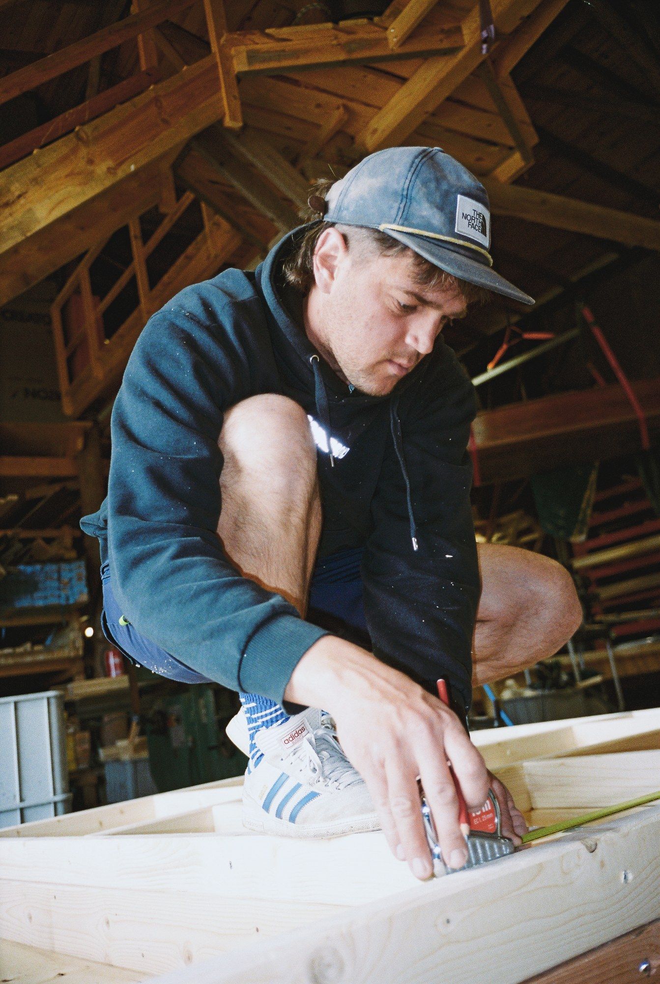 Ein Handwerker hockt auf dem Bodenrahmen und reißt mit Bleistift und Maßband an
